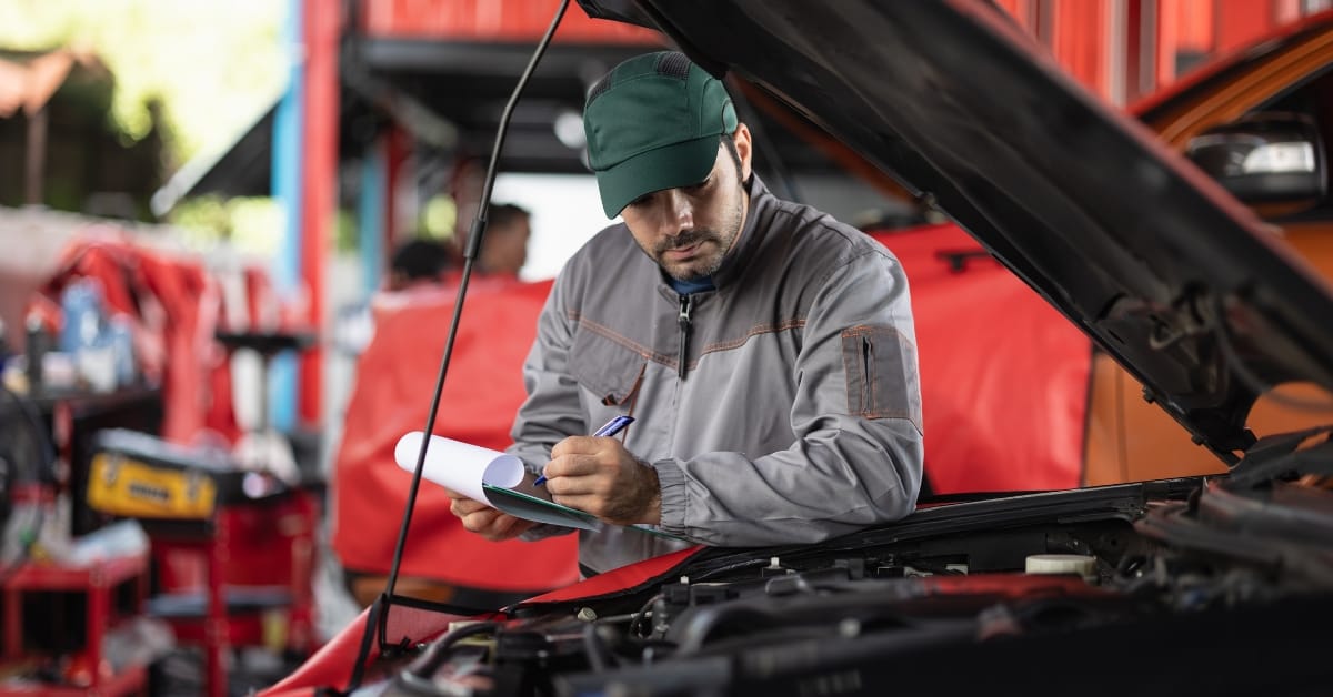MOT inspector writing notes while checking under a car bonnet