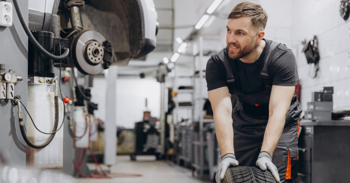 Mechanic carrying a car tyre in a busy garage