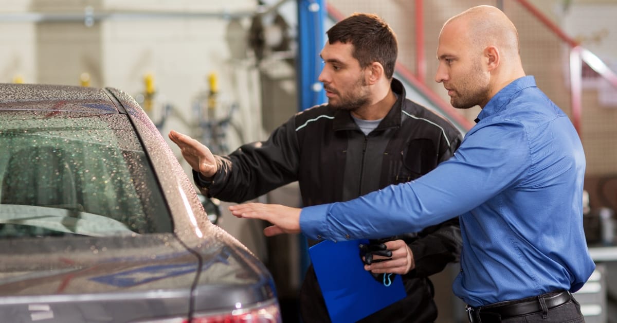 Mechanic and customer inspecting the back of a car together in a garage