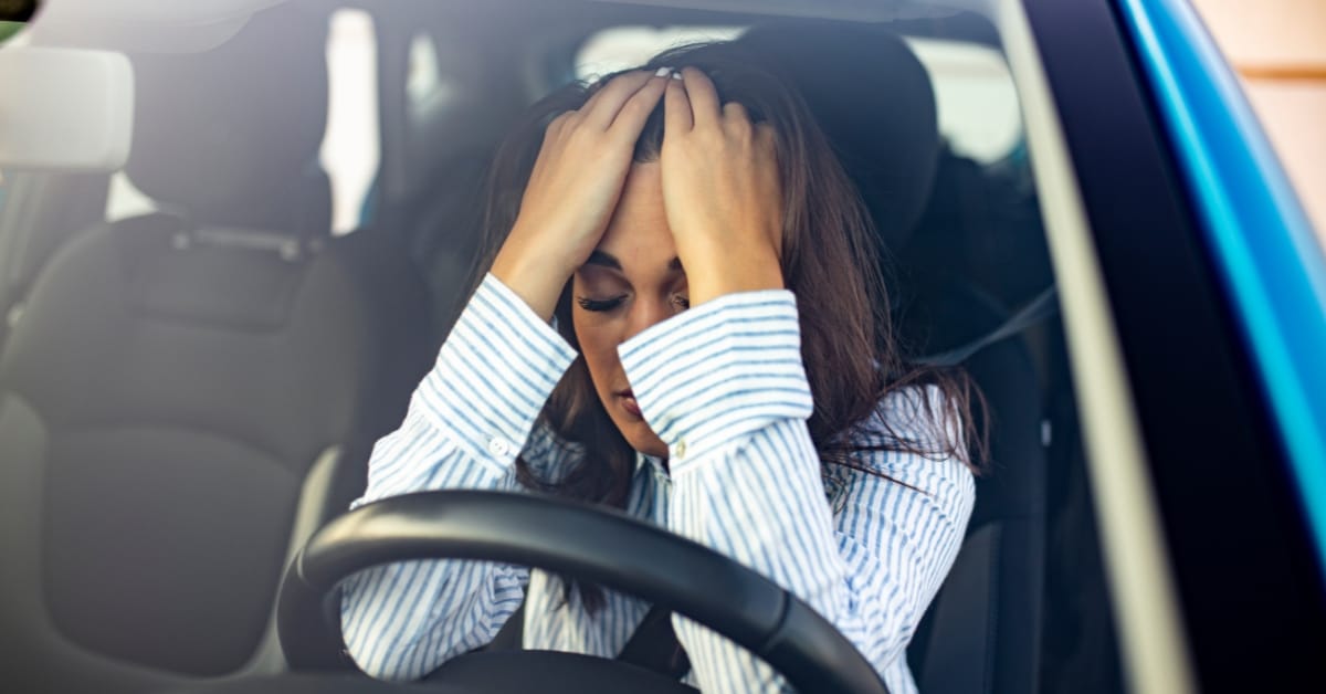 Woman in car appearing stressed with hands on her head