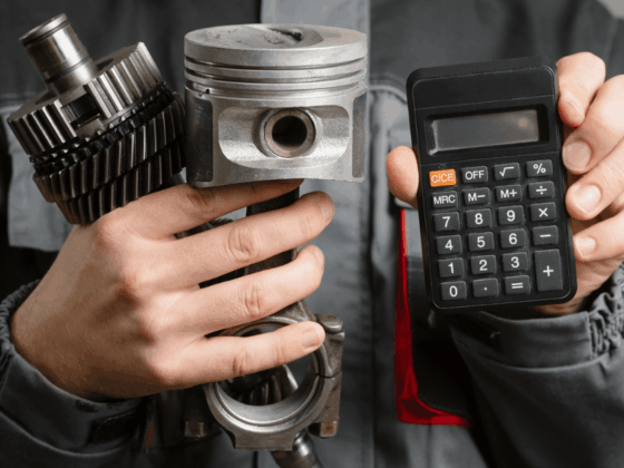 Mechanic holding car engine parts and a calculator, representing increasing car repair costs.