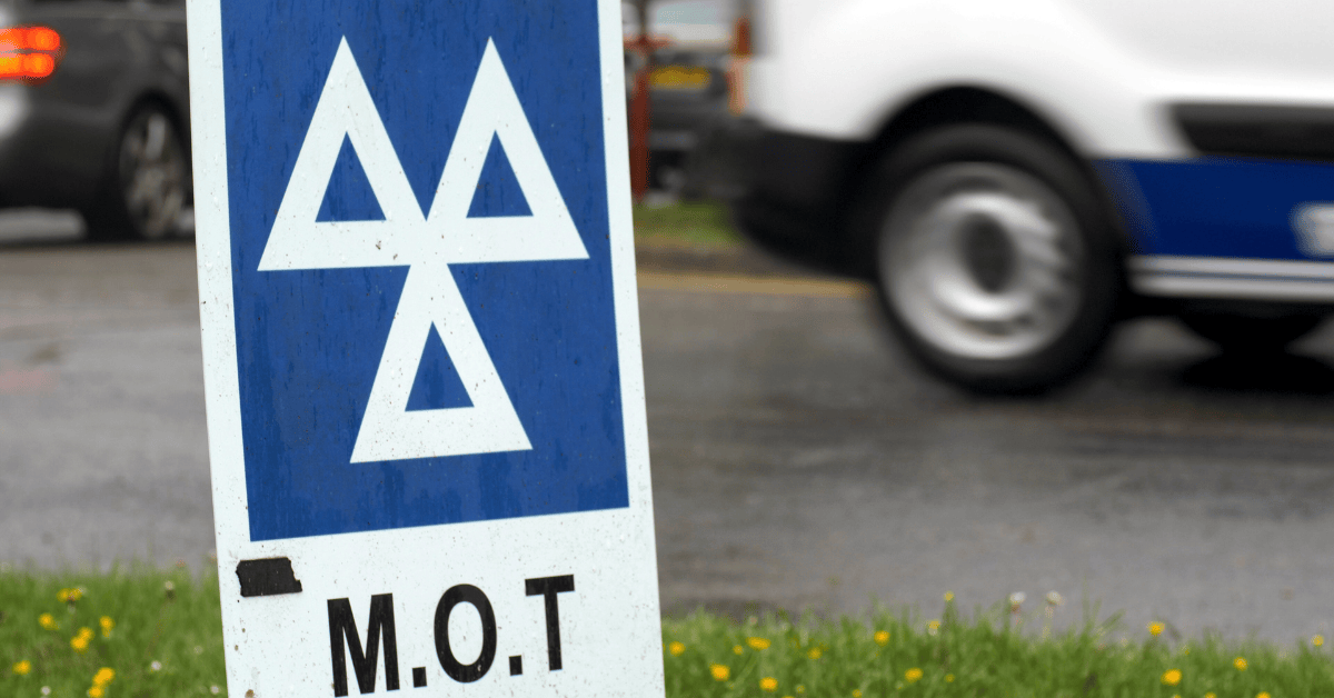 Close-up of MOT sign with passing vehicle in the background, representing MOT costs of running a car.