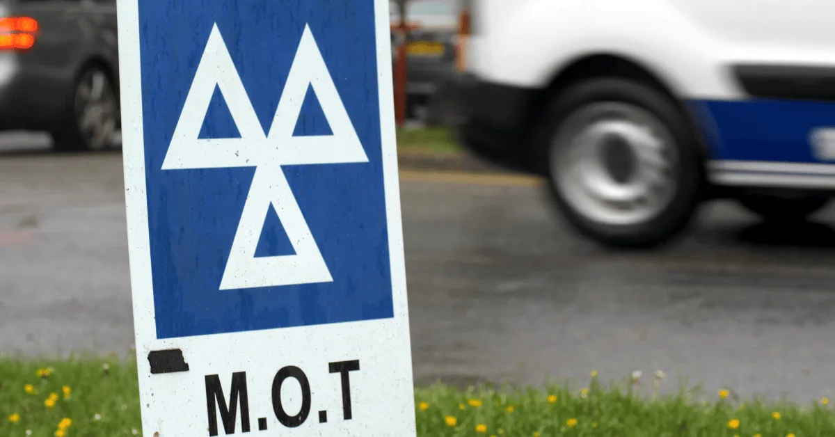 Close-up of MOT sign with passing vehicle in the background, representing MOT costs of running a car.