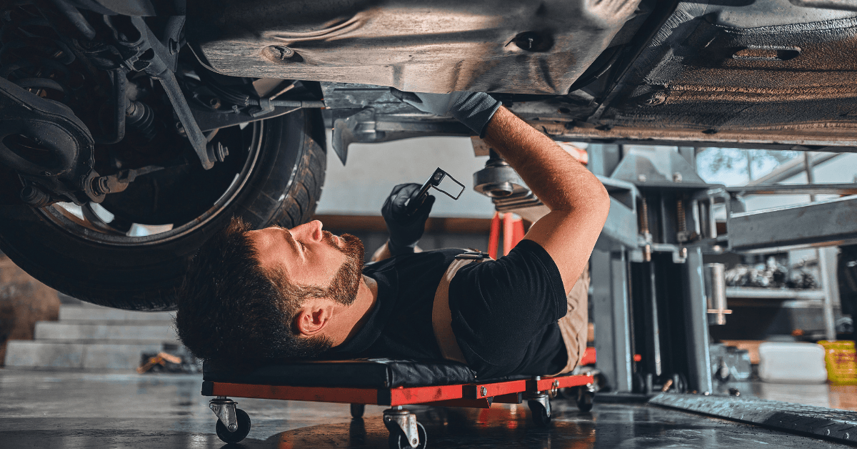Mechanic lying on a creeper working underneath a vehicle in a garage, representing car repair garages offering buy now pay later options
