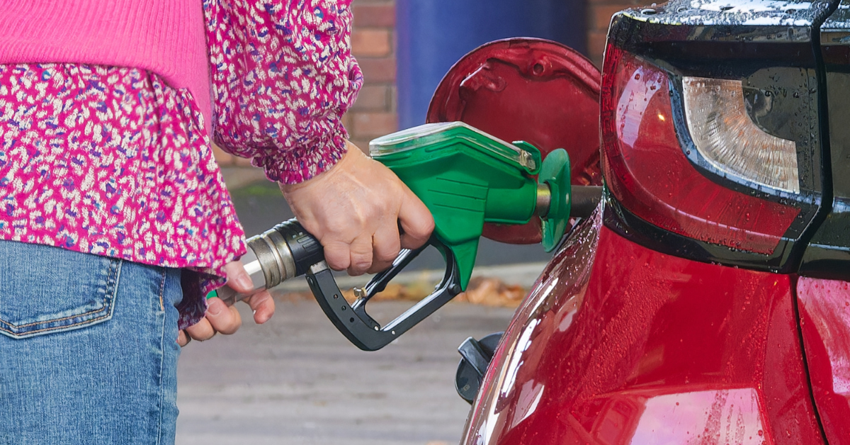 Person refuelling a red car with green petrol pump nozzle, representing cost of running a car and fuel expenses.