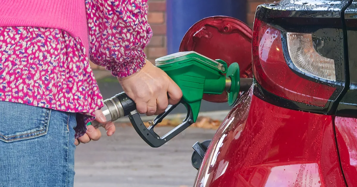 Person refuelling a red car with green petrol pump nozzle, representing cost of running a car and fuel expenses.