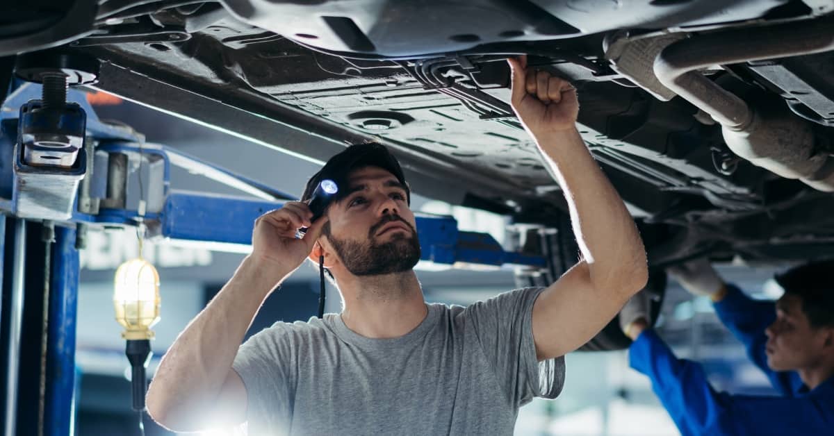 Mechanic inspecting the underside of a car in a workshop, highlighting the cost of car repairs and flexible BNPL payments.