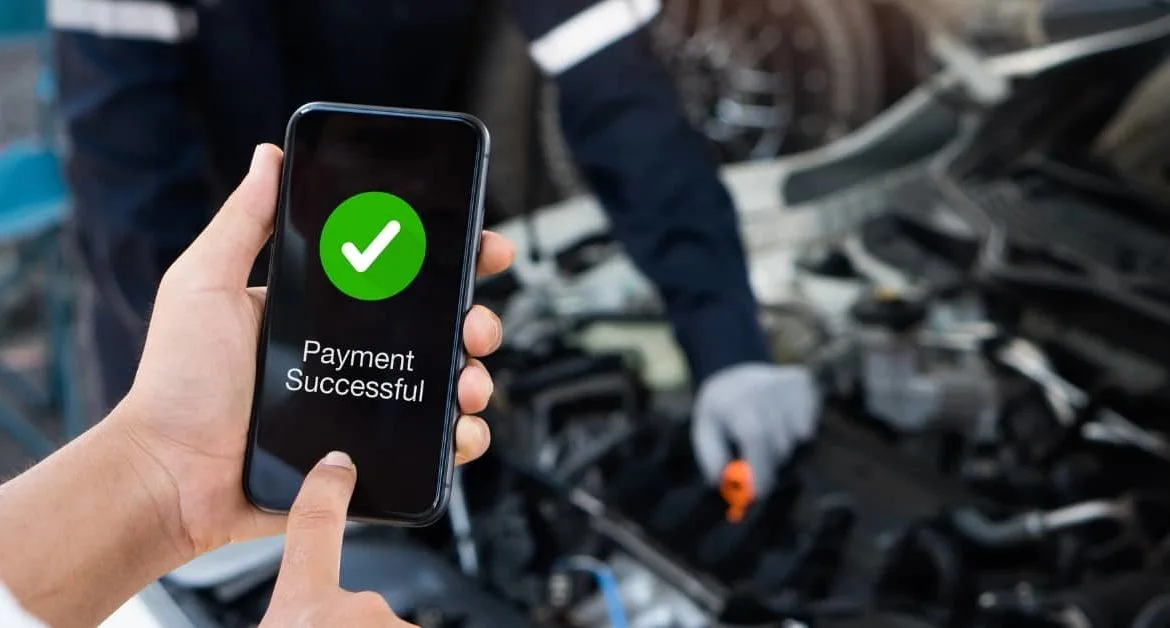 and holding a smartphone showing a successful payment screen, illustrating interest-free car repair finance through BNPL services.