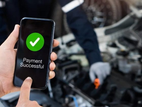 and holding a smartphone showing a successful payment screen, illustrating interest-free car repair finance through BNPL services.