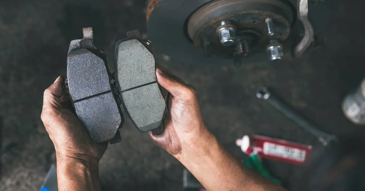Mechanic comparing worn and new brake pads during car maintenance, highlighting how regular servicing extends the lifespan of a car and reduces unexpected car repairs.