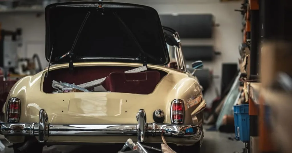 Classic cream car with open boot in a workshop, showing the impact of car repairs on the lifespan of a car, particularly for older vehicles facing higher maintenance needs.