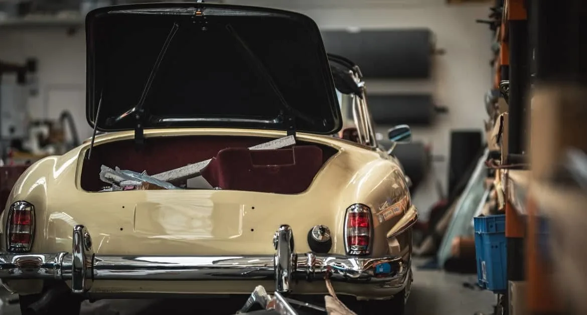 Classic cream car with open boot in a workshop, showing the impact of car repairs on the lifespan of a car, particularly for older vehicles facing higher maintenance needs.