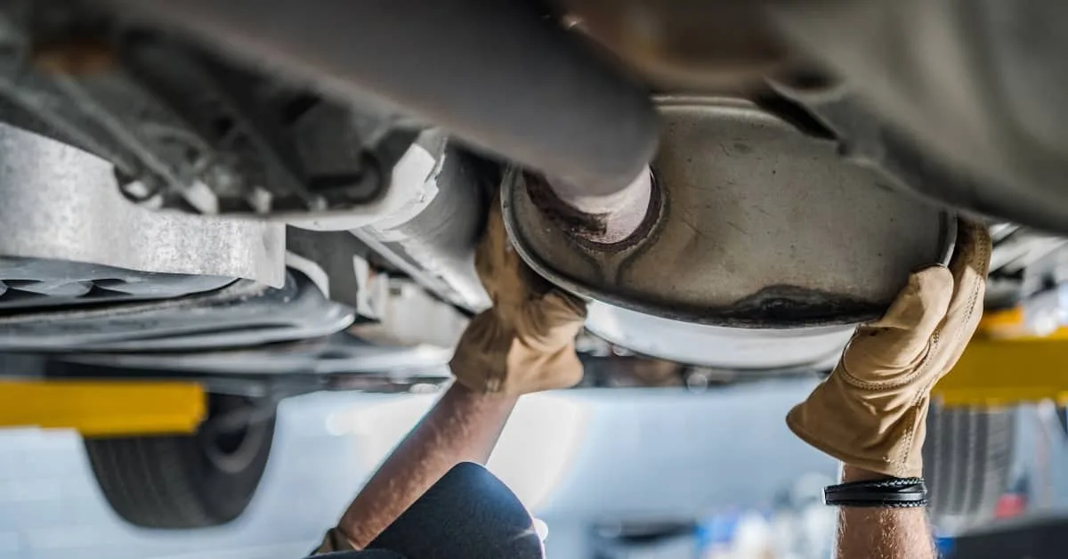 Mechanic wearing gloves working under a vehicle to repair a catalytic converter, one of the common car repairs that can drive up the cost of car repairs without proper car repair finance support.