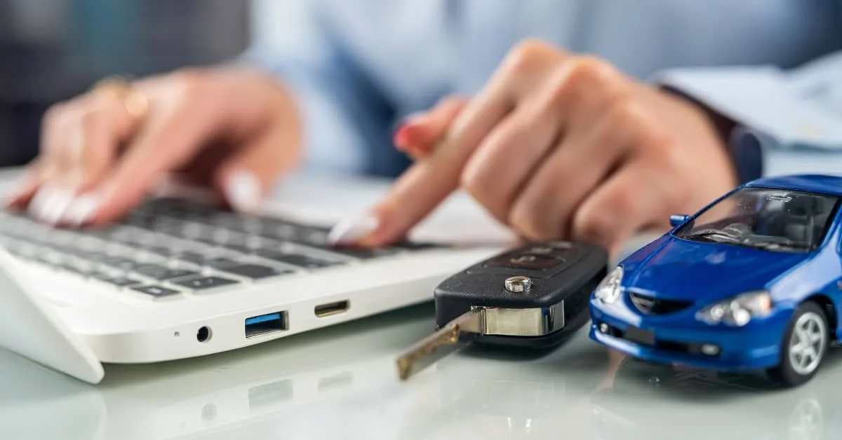 Close-up of a person using a laptop beside car keys and a toy car, representing the rising cost of living and financial pressures of car repairs and how budgeting affects the lifespan of a car.