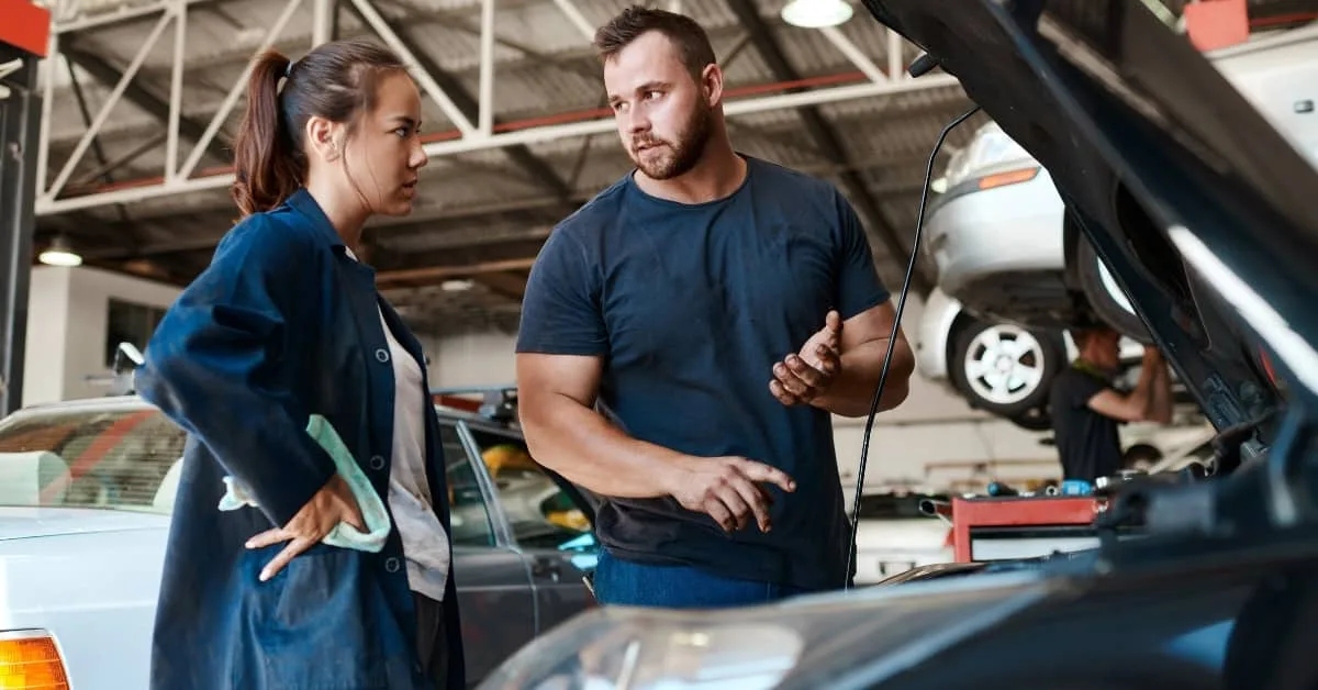 Mechanic discussing car servicing and young driver repairs with a female driver in the garage.