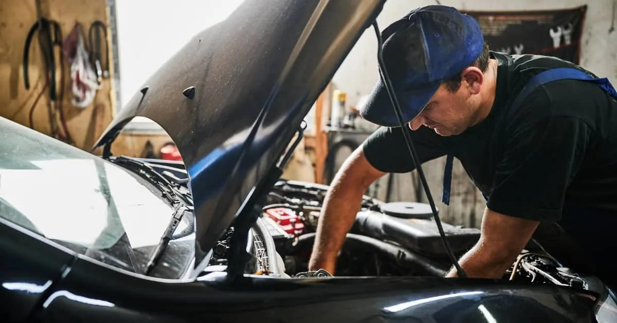 Mechanic leaning over a car engine in a workshop, carrying out engine repairs that highlight the growing cost of car repairs and the value of car repair finance options.