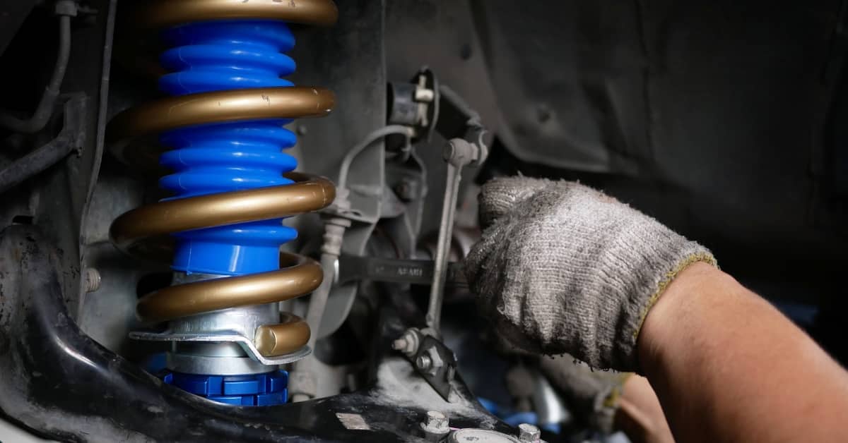 Mechanic adjusting a car’s suspension system with a bright blue spring, representing common car repairs that impact driving safety and contribute to the cost of car repairs.