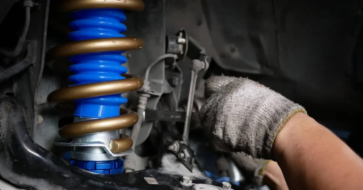 Mechanic adjusting a car’s suspension system with a bright blue spring, representing common car repairs that impact driving safety and contribute to the cost of car repairs.