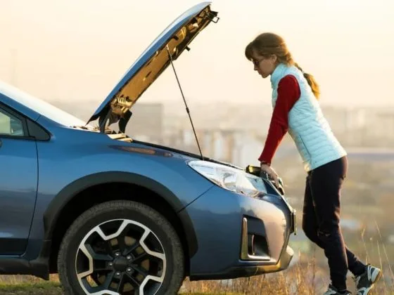Young driver delaying car repairs while checking a broken-down vehicle, concerned about car repair costs.