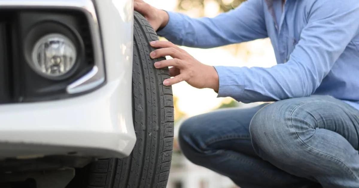 Driver carrying out car servicing by inspecting tyre condition and tread wear at home.