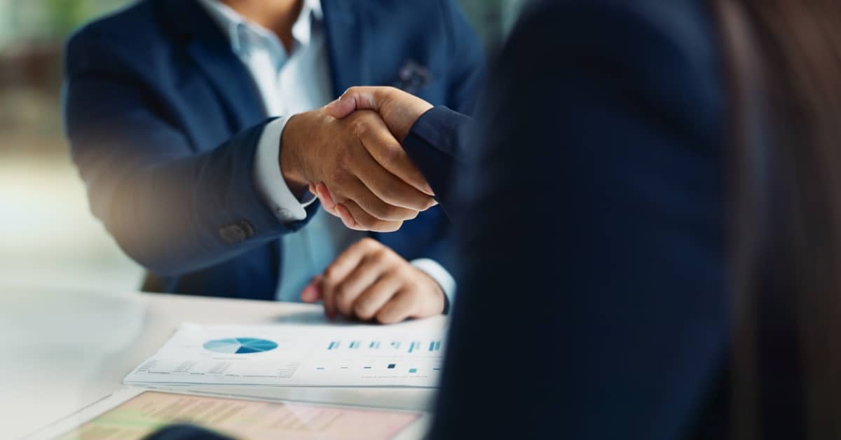 Business professionals shaking hands over financial documents after agreeing flexible business finance options.
