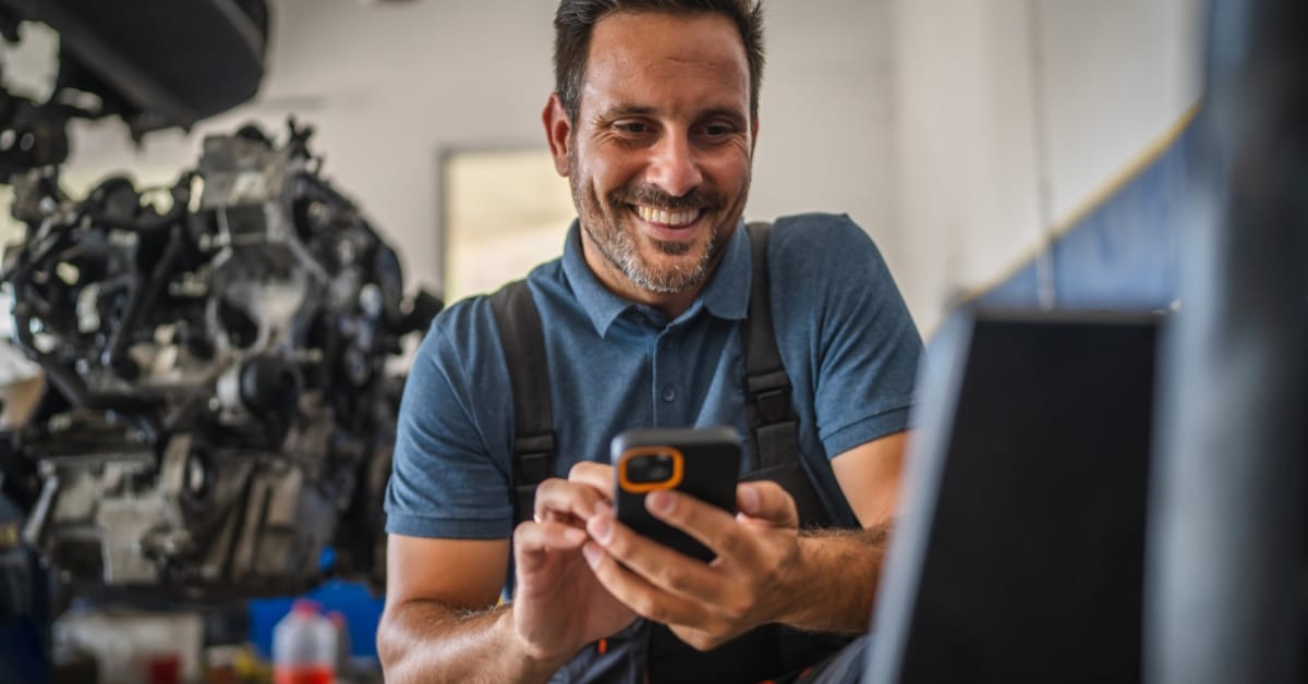 Mechanic checking a mobile phone in a garage while offering a car repair payment plan with flexible car repair monthly payments and pay later car repairs through car service finance.