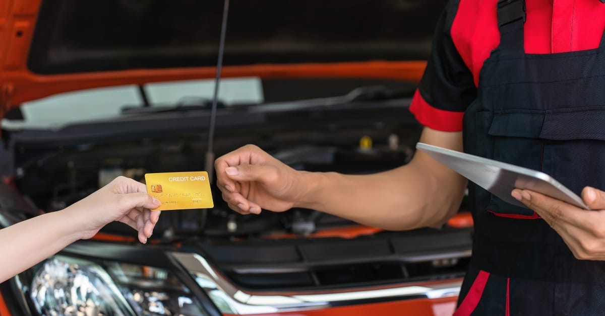 A customer hands over a card for repairs as a mechanic prepares an invoice, reflecting the impact of the 2025 Budget on garage labour rates and overall motoring costs.