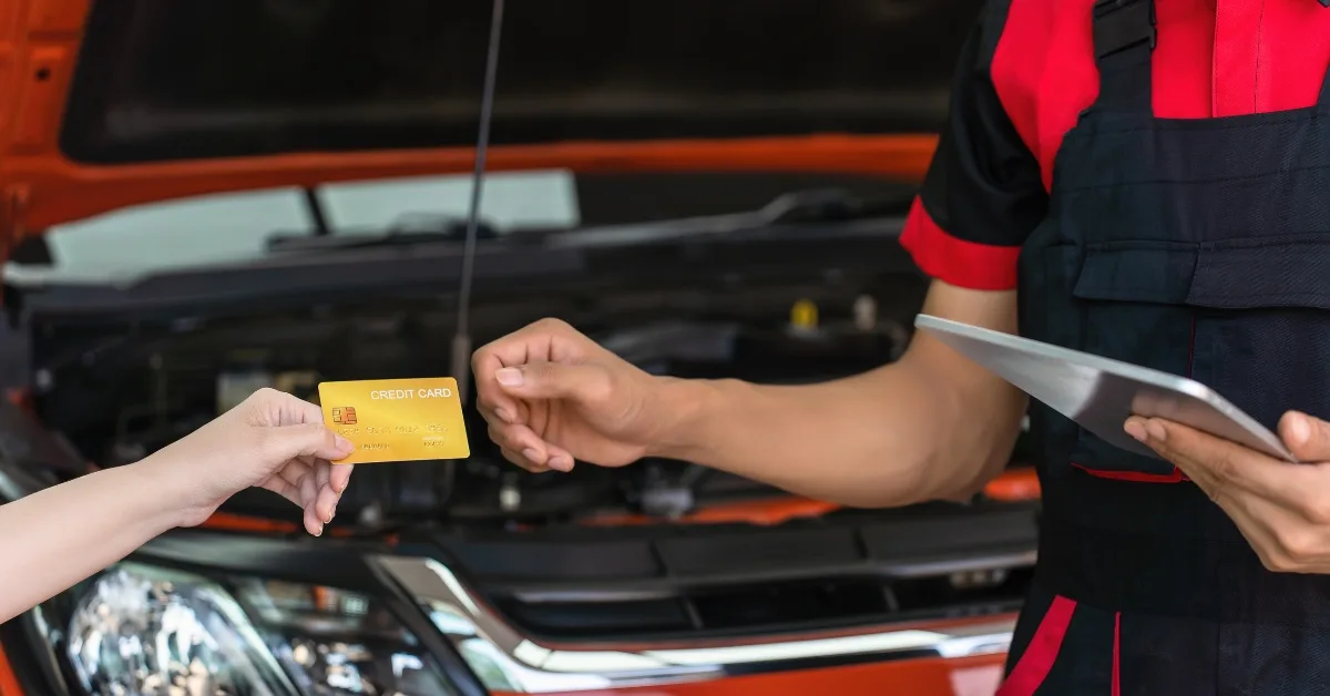 A customer hands over a card for repairs as a mechanic prepares an invoice, reflecting the impact of the 2025 Budget on garage labour rates and overall motoring costs.