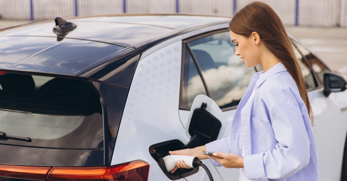 A driver charges an electric vehicle while thinking about how the 2025 UK Budget may affect motoring costs and the wider automotive sector.