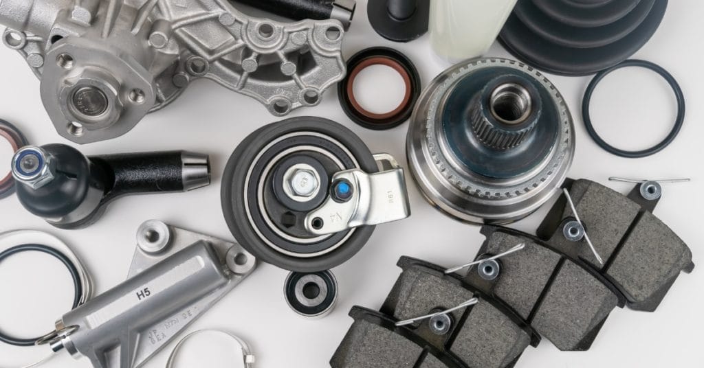Car parts shortage: Flat lay of assorted car parts including brake pads, bearings and mechanical components laid out on a white background.