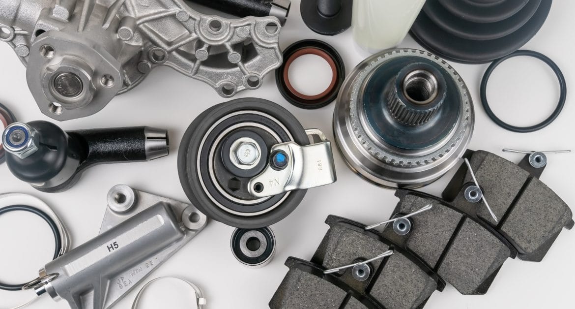 Car parts shortage: Flat lay of assorted car parts including brake pads, bearings and mechanical components laid out on a white background.