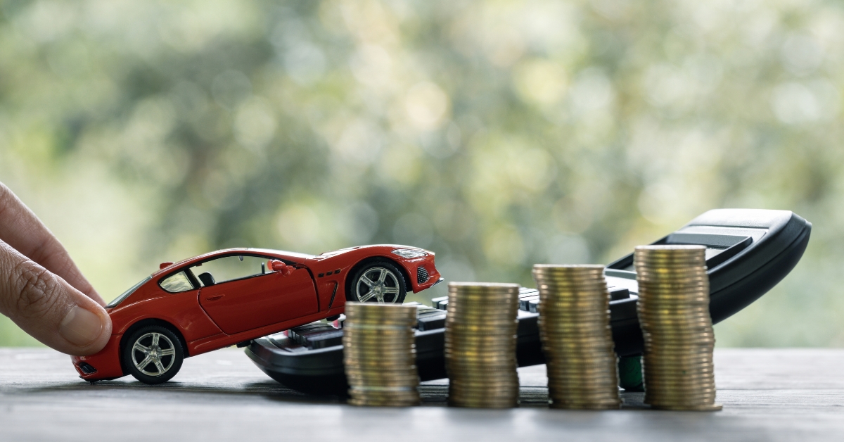 Car servicing costs, Red toy car positioned on top of a calculator beside stacks of coins, representing rising car servicing costs and vehicle maintenance expenses.