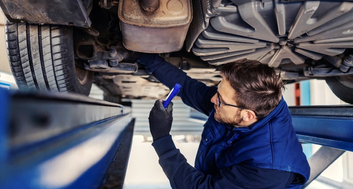 UK skills shortage: A mechanic wearing protective glasses inspecting a vehicle on a lift while taking notes, highlighting skilled labour in a workshop environment.
