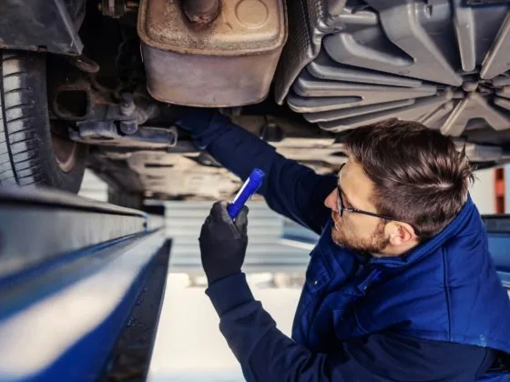 UK skills shortage: A mechanic wearing protective glasses inspecting a vehicle on a lift while taking notes, highlighting skilled labour in a workshop environment.