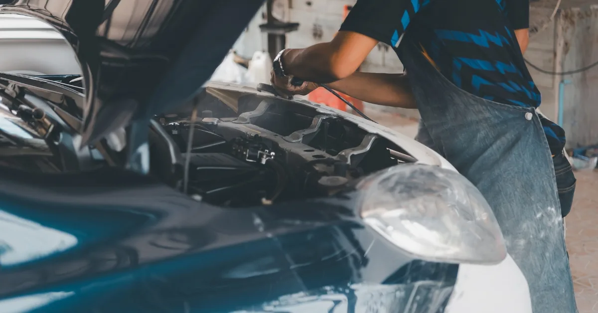 Why car write-offs are increasing: A mechanic working under the bonnet of a car in a workshop, carrying out repairs on a vehicle with the hood open.