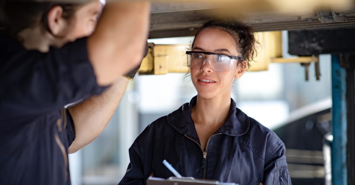 mechanic labour rates: A mechanic working underneath a raised car using a torch to inspect the vehicle’s underside.