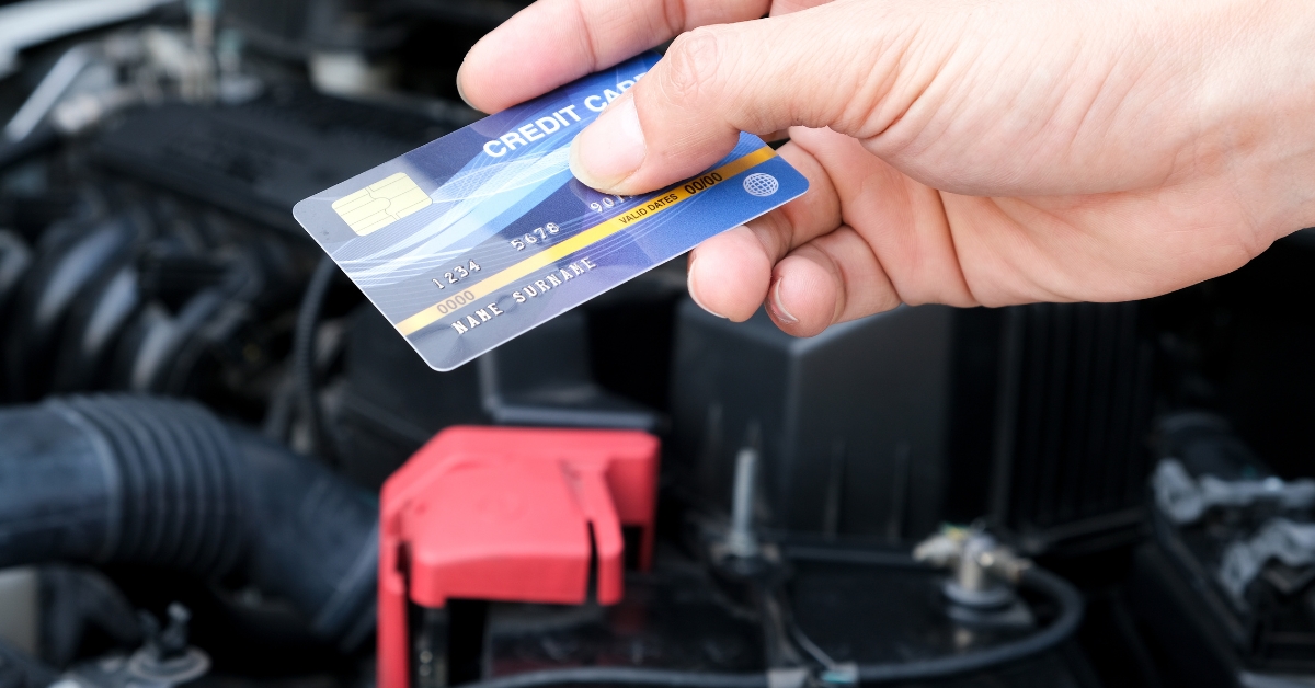 Interest-free car repairs, Hand holding a credit card in front of an open car bonnet, representing interest-free car repairs and flexible payment options.