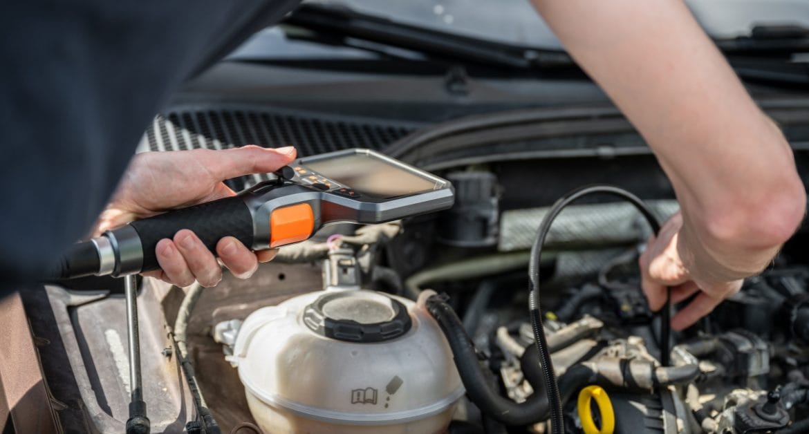 Preventative car maintenance, Mechanic using a diagnostic tool under a car bonnet, illustrating preventative car maintenance checks and inspections.