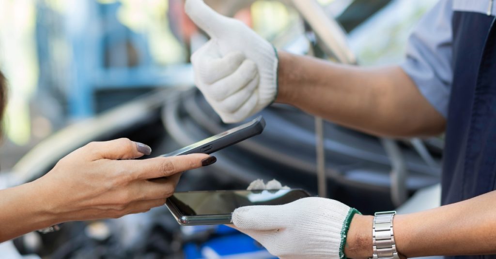 Responsible BNPL for car repairs, Mechanic giving a thumbs up while a customer holds a smartphone, symbolising responsible BNPL for car repairs and digital payment approval.