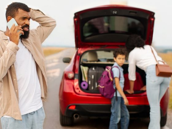 Car repair help for families – Parent on the phone beside a broken-down car while family members stand at the open boot.