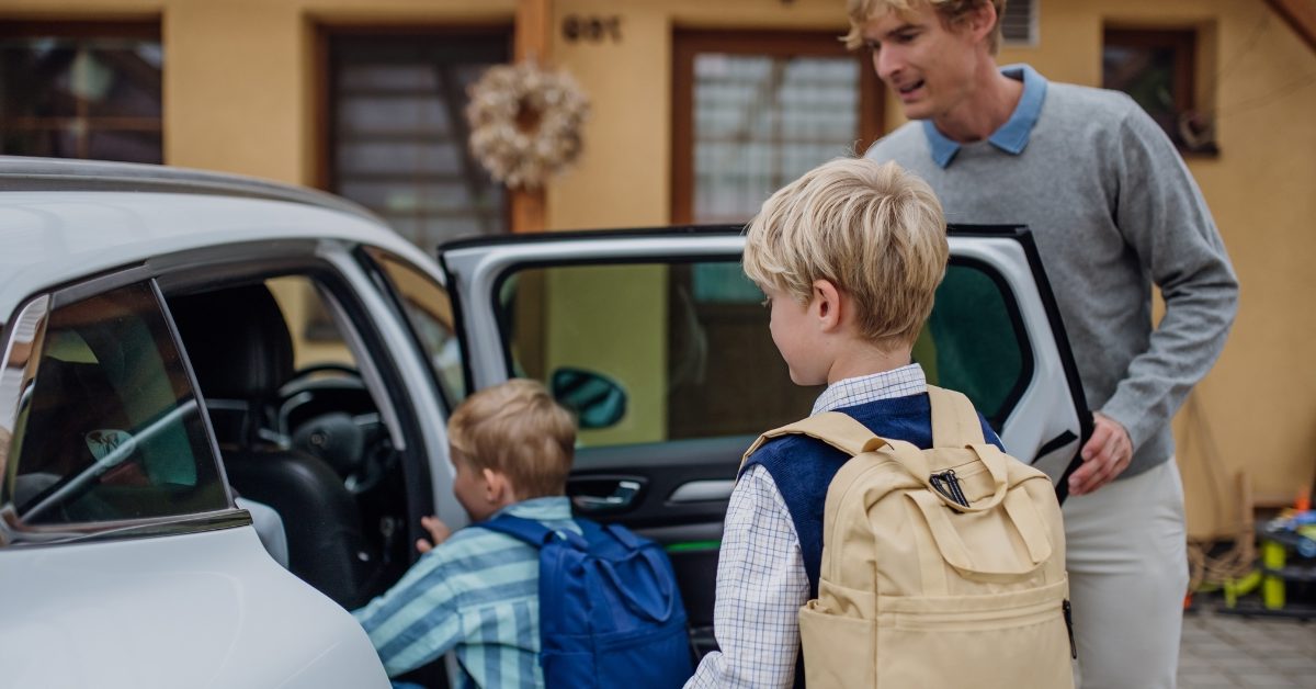 Finance for essential car repairs – Adult helping two children get into a car outside a house.