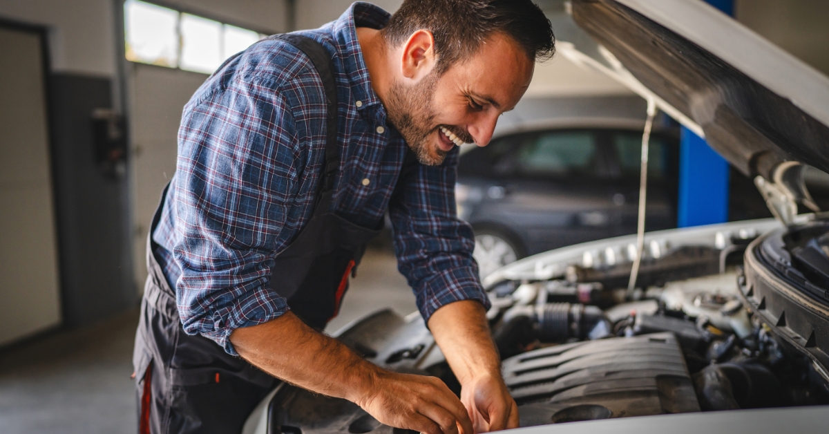 finance for car repairs – Mechanic smiling while working under the bonnet of a car in a garage.